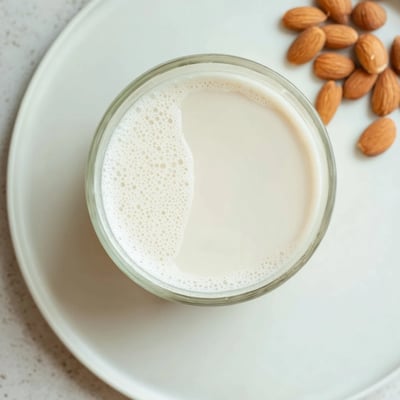 Pouring fresh white almond milk from glass jar into clear drinking cup