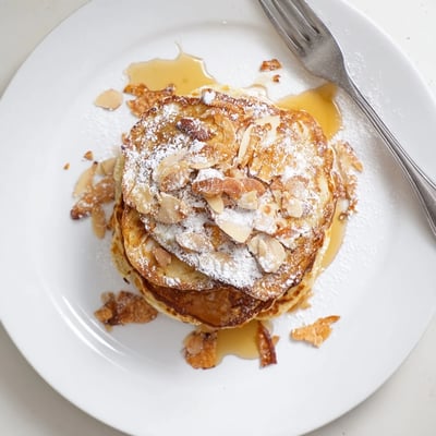 Golden almond croissant protein pancakes drizzled with maple syrup on a white breakfast plate